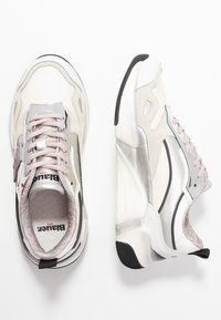 Zapatillas deportivas en blanco y plata con un diseño voluminoso, acentos de malla texturizada y cordones en rosa claro. Suela de goma negra y logotipo visible.