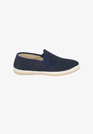 Zapato azul marino sin cordones con perforaciones cuadradas, suela blanca texturizada y diseño de perfil bajo sobre un fondo blanco.