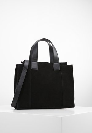 Černá semišová taška typu tote s hladkými koženými doplňky. Má dvě horní ucha a odnímatelný ramenní popruh. Obdélníkový tvar, minimalistický design.