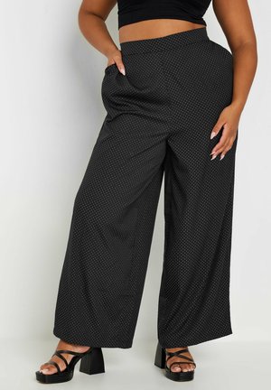 Wijdvallende zwarte broek met witte stippen, een soepele textuur en een hoge tailleband. Gecombineerd met zwarte platform sandalen.
