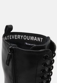 Mustat nahka nilkkasaappaat, joissa on nauhat, vetoketjukiinnitys sivussa ja pehmustettu nilkkaosa, jossa on "WHATEVERYOUWANT"-teksti sisäpuolella.