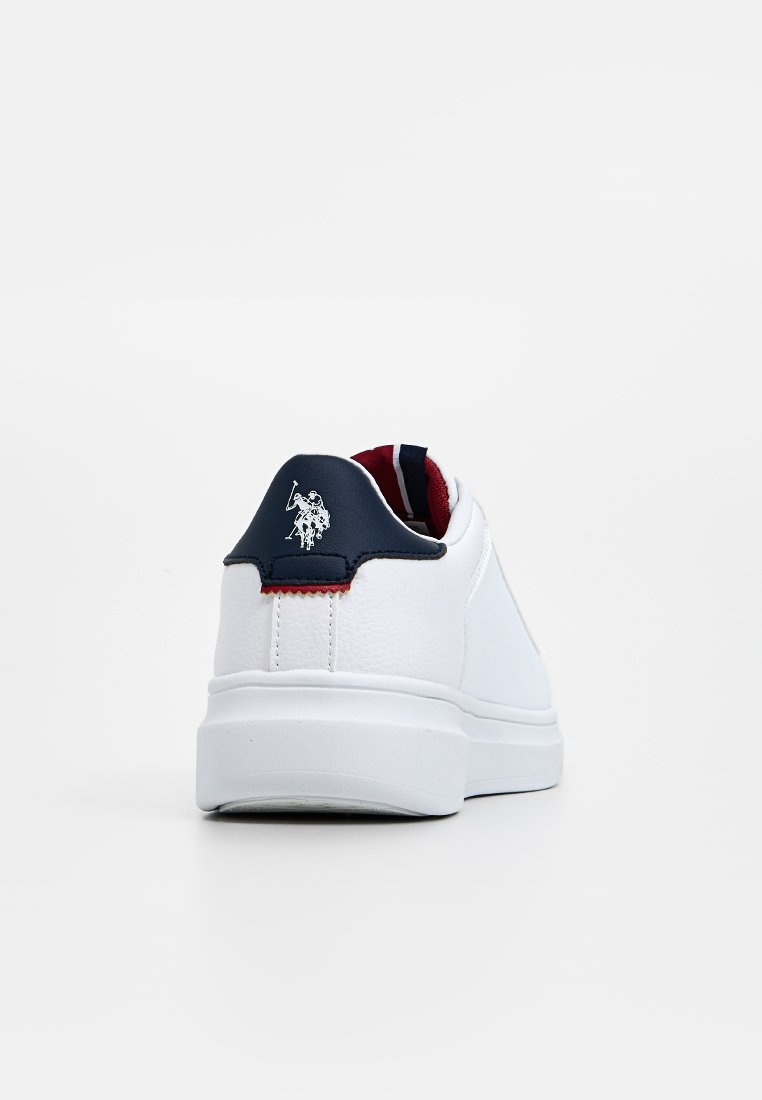 Zapatilla blanca con parte superior de cuero texturizado, detalle en el talón en color marino, pestaña de acento roja y un logo embosado en la parte trasera. Suela plana de goma.