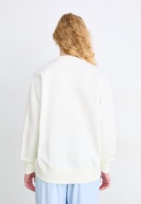 Sudadera blanca de corte relajado, con cuello redondo y puños acanalados. Presenta una textura suave y un diseño minimalista, vista desde la parte de atrás.