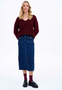 Burgundská mäkká sveter s výstrihom do V, skombinovaný s tmavomodrou midi sukňou z denimu so predným rozparkom a dvoma zadnými vreckami. Čierne platformové topánky.