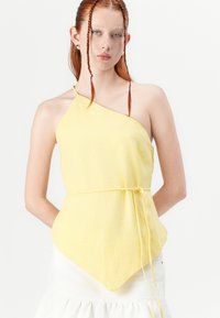 Asymmetrical yellow top with a textured finish, single shoulder strap, and a tied waist, featuring a pointed hemline.