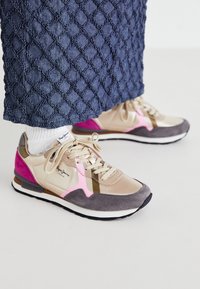 Beiga och rosa sneakers med mocka och syntetiska material. Har en rosa accent, grå mocka tåhätta och guldfärgad hårdvara. Snörning.
