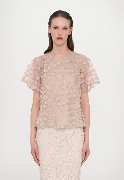 Beige floral embroidered top with short, sheer sleeves and a round neckline; fabric appears delicate with a textured, layered design.