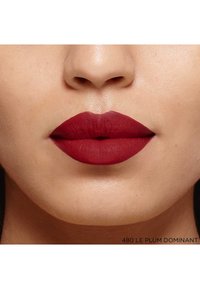 Rouge à lèvres mat rouge profond appliqué sur des lèvres pleines, mettant en valeur une texture lisse et une forme bien définie, avec une touche d'un fond de teint naturel.