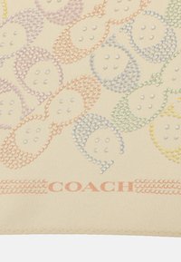 Zijde sjaal in crème met meerkleurige rhinestone patronen die op vissen lijken, met de merknaam "COACH" langs de onderkant.