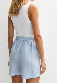 Vaaleansiniset shortsit joustavalla vyötärönauhalla, valmistettu pehmeästä kankaasta, rento malli ja yksinkertainen design. Ei näkyviä kuvioita tai koristeita.