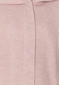 Tissu rose clair avec une texture douce, présentant une couture au centre et un col arrondi. Le matériau semble extensible et confortable.