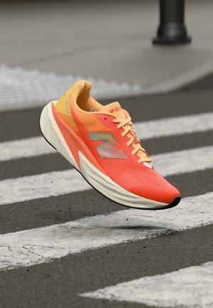 Scarpa da corsa New Balance di un arancione e giallo brillante sospesa a mezz'aria sopra un attraversamento pedonale in città.