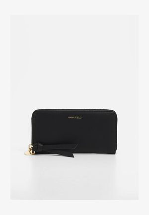 Black zip-around wallet made of smooth synthetic material, featuring a gold logo and a decorative tassel with a metal charm.