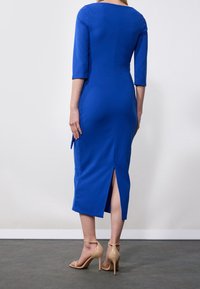 Bodycon-klänning i starkblått tyg, knä-lång med trekvartslånga ärmar och slits bak. Matchad med nakna högklackade sandaler.