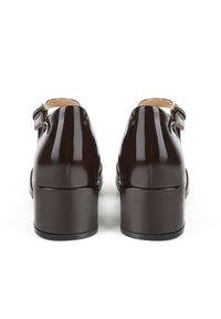 Talons en cuir verni marron avec une texture lisse, un bout arrondi, un talon carré et une bride de cheville avec un détail de boucle métallique.