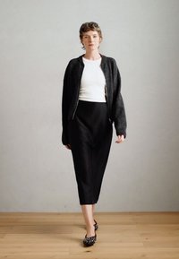 Czarna midi spódnica o gładkiej teksturze i wysokim stanie, zestawiona z dopasowaną białą bluzką oraz ciemną wełnianą bomberką. Białe baleriny w kropki.