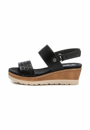 Sandalia de cuña negra con tira perforada, correa ajustable en el tobillo y suela de cuña de color marrón claro con base beige y tread texturizado.