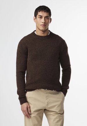 Brun stickad tröja med ribbad rund halsringning och långa ärmar, som har en mjuk textur. Kombinerad med beige byxor.