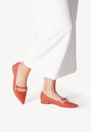 Coral patent leather flats with a pointed toe, featuring a circular cutout and metallic accent, worn with white pants.