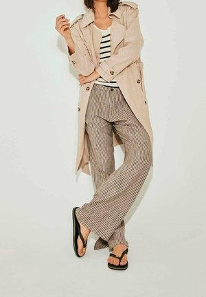 Beige trench coat with buttons, striped tank top, striped wide-leg pants, and black flip-flops. Smooth fabric and relaxed fit throughout.