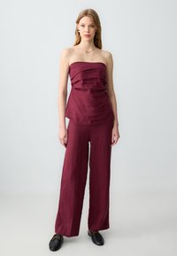 Completo bordeaux composto da due pezzi con top drappeggiato senza spalline e pantaloni a gamba larga realizzati in tessuto testurizzato con vestibilità comoda e senza chiusure visibili.