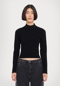 Svart ribbad polotröja med långa ärmar och cropat avslut som kombineras med högmidjade mörkjeans. Slät textur och åtsittande design.