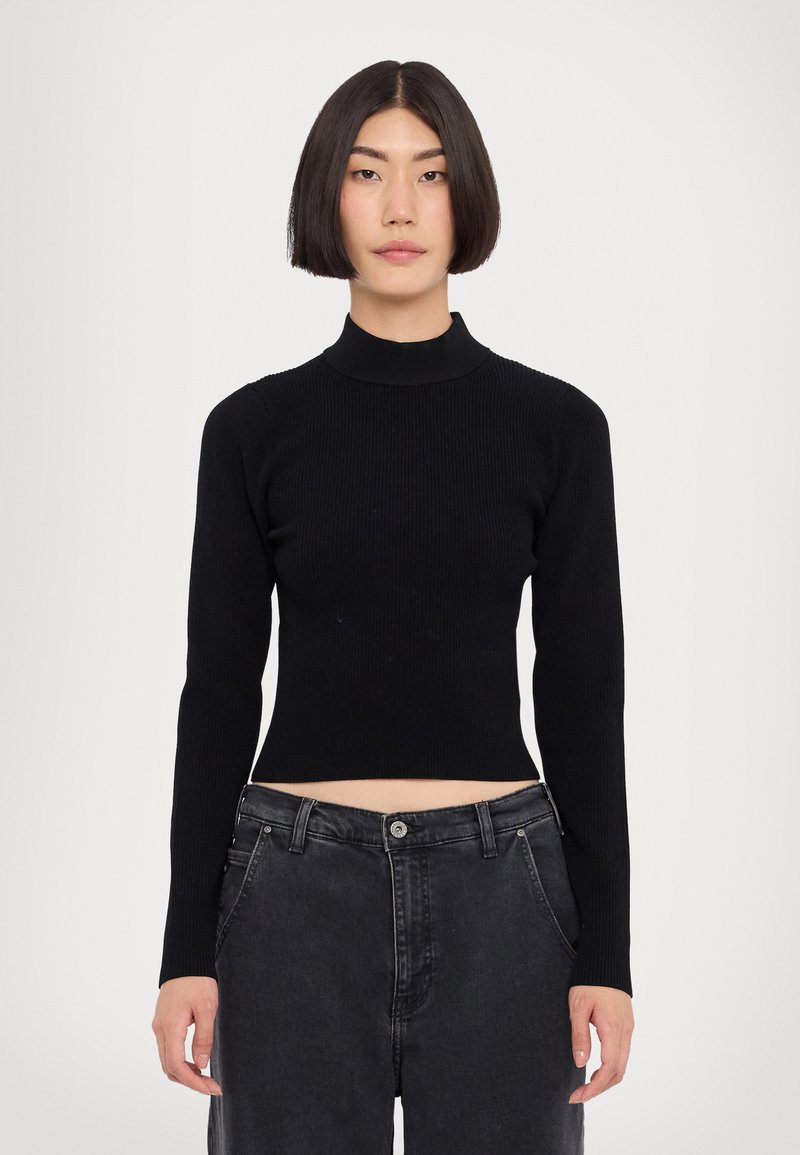 Svart ribbad polotröja med långa ärmar och cropat avslut som kombineras med högmidjade mörkjeans. Slät textur och åtsittande design.