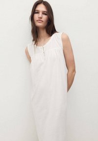 Abito bianco in cotone con design senza maniche, caratterizzato da un corpino testurizzato, una chiusura con bottoni e una silhouette ampia e lievemente svasata.