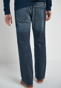 Donkerblauwe denim jeans met een rechte pijp, voorzien van twee achterzakken, zichtbare stiksels en een soepele textuur.