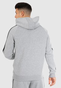 Grijze hoodie met een zachte textuur, voorzien van een capuchon, zwarte zijstrepen en geribbelde boorden en zoom. Alleen de achterkant is zichtbaar, er zijn geen details van de voorkant te zien.