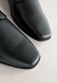 Fekete bőr elegáns cipők hegyes orral, sima textúrával és minimális varrási részletekkel. Elegáns, fényes felülettel rendelkezik.