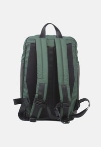 Grüner Nylon-Rucksack mit gepolsterten schwarzen Netzträgern, einem oberen Griff und verstellbaren Seitenlaschen, der ein elegantes, funktionales Design bietet.