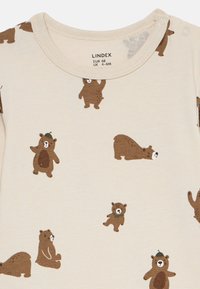 Beige baby romper med bruna björnar i olika poser tryckt, med tryckknappar på axeln för enkel påklädning, storlek 4-6 månader.