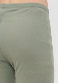 Primo piano di una persona che indossa pantaloni in tessuto a coste verde chiaro, con un focus sulla vita e sull'area dei fianchi.