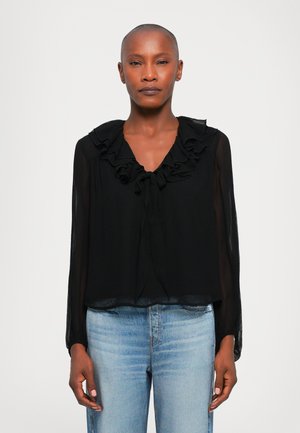 Zwarte blouse met een gerimpelde kraag en strikken bij de halslijn. Lange, doorschijnende mouwen met een losse pasvorm. Gecombineerd met lichte jeans.