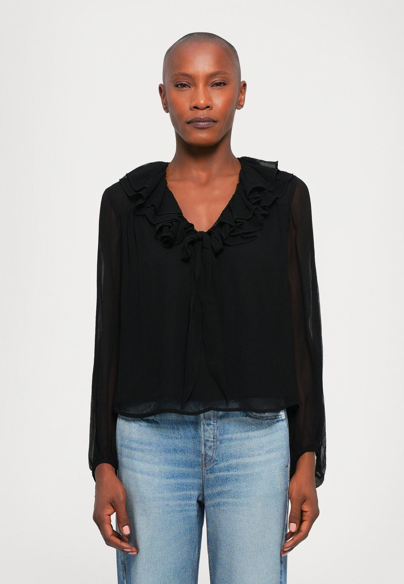 Zwarte blouse met een gerimpelde kraag en strikken bij de halslijn. Lange, doorschijnende mouwen met een losse pasvorm. Gecombineerd met lichte jeans.