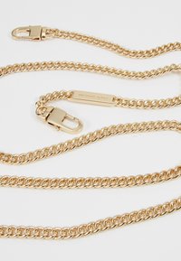 Náhrdelník zlaté barvy s řetízkem, který se skládá z propletených článků a zapínání, s obdélníkovou destičkou, na které je vyryto "Michael Kors." Hladký povrch.