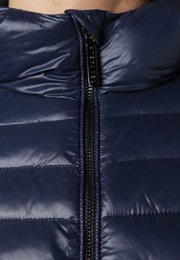 Granatowa puchowa kurtka z wysokim kołnierzem, o połyskującej fakturze i centralnym zamkiem błyskawicznym. Poziomy pikowany wzór.