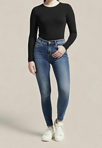 Vaqueros pitillo de talle alto en denim azul con desgaste, combinados con una camiseta negra de manga larga y zapatillas blancas, posando frente a un fondo neutro.