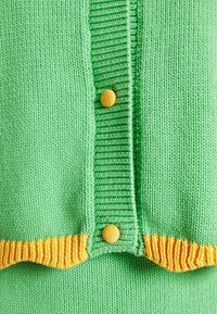 Gros plan sur un tissu tricoté vert avec un bord jaune et deux boutons recouverts de tissu jaune sur une patte côtelée.
