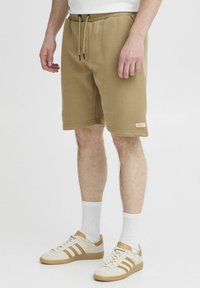 Brune bomullsblandingsshorts med elastisk midje og snor. Har sidelommer og en liten logomerke på kanten.