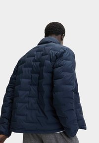 Chaqueta de plumas azul marino con un patrón acolchado, cuello alto y puños elásticos, que proporciona una apariencia texturada e insulated.