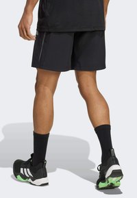 Sorte atletiske shorts i et let materiale, med en lige pasform og glat tekstur. Sorte sokker og sneakers med grønne accenter.