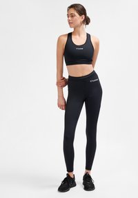 Svart atletisk sport-bh och leggings-set gjort av elastisk, slät tyg. Har logotypdetaljer och en figurnära passform.