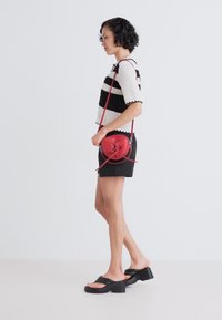 Haut à manches courtes noir et blanc rayé, shorts noirs et sac à bandoulière rond rouge, associés à des sandales noires à semelles épaisses.