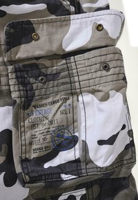 Cargo bukser med camouflage-mønster, der har nuancer af grå og hvid. Inkluderer en vintage label med blå tryk og metalknapper.