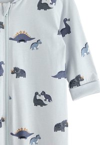 Lysblå pyjamas med dinosaur mønster i mørkegrå og marineblå, med en frontlynlås og manchetter ved ærmerne for ekstra detalje.