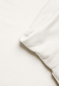 Helles beigefarbenes Sweatshirtgewebe, glatte Textur, an den Ärmeln gefaltet, mit einem subtilen Strickmuster. Einfaches Design ohne sichtbare Beschläge.