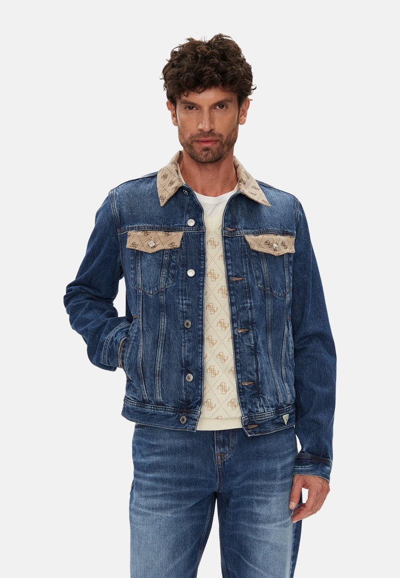 Chaqueta de mezclilla con cuello de pana color beige y bolsillos en el pecho. Presenta tonos azules, cierre de botones y contrasta con un suéter de crema con estampado debajo.