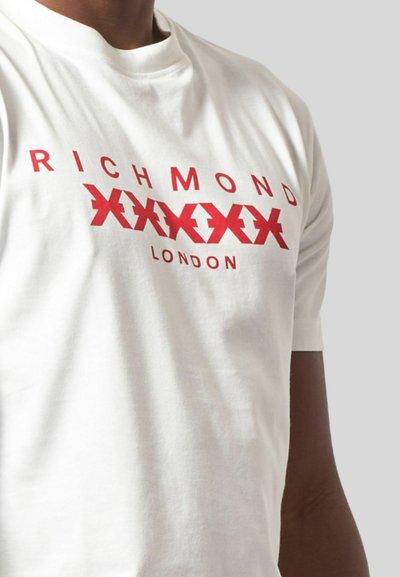 T-shirt bianca in cotone con testo grafico rosso "RICHMOND" e "LONDON", e un motivo a zigzag ripetuto sul petto. Maniche corte.